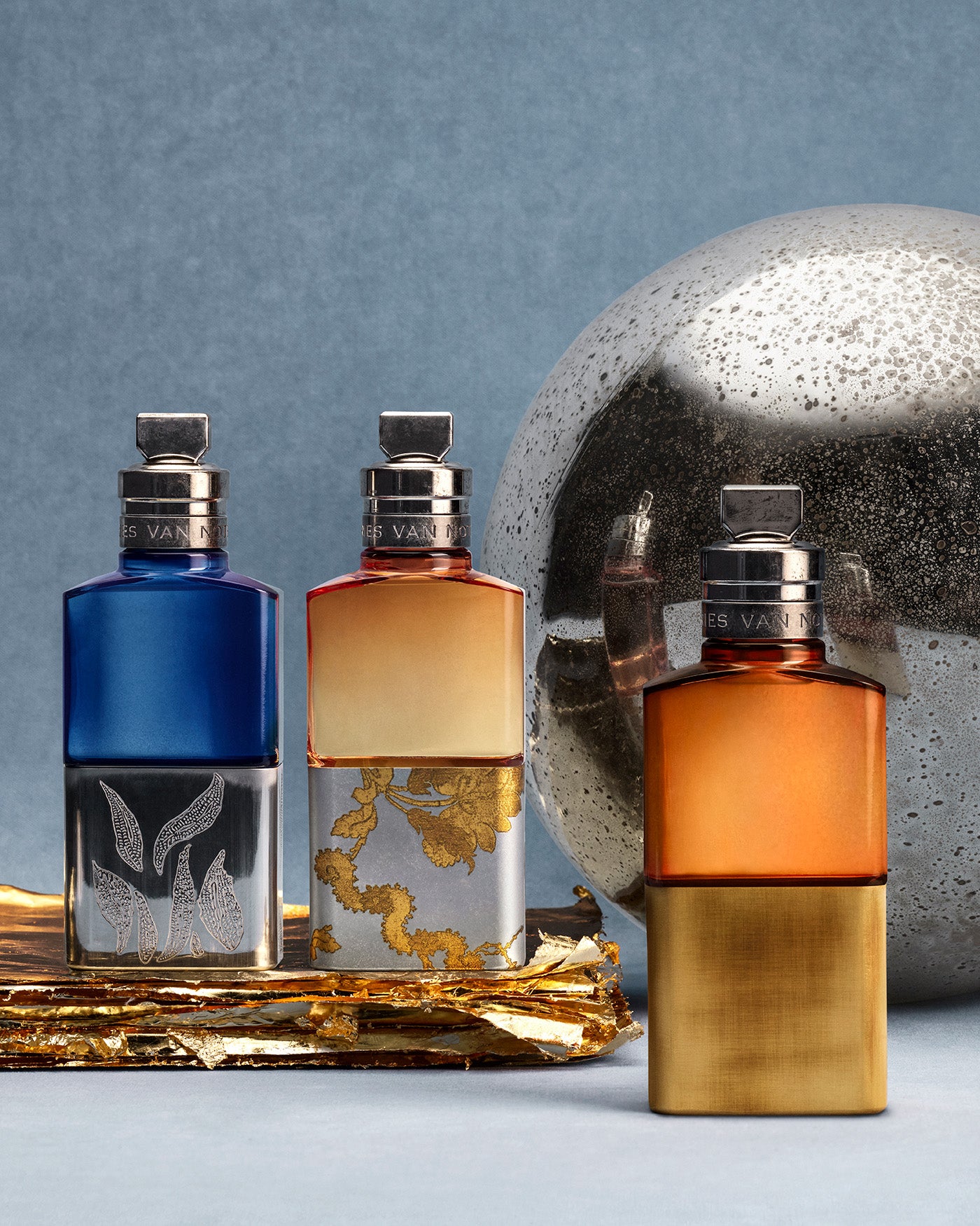 Three perfume bottles with metallic caps on a reflective surface with a gray background