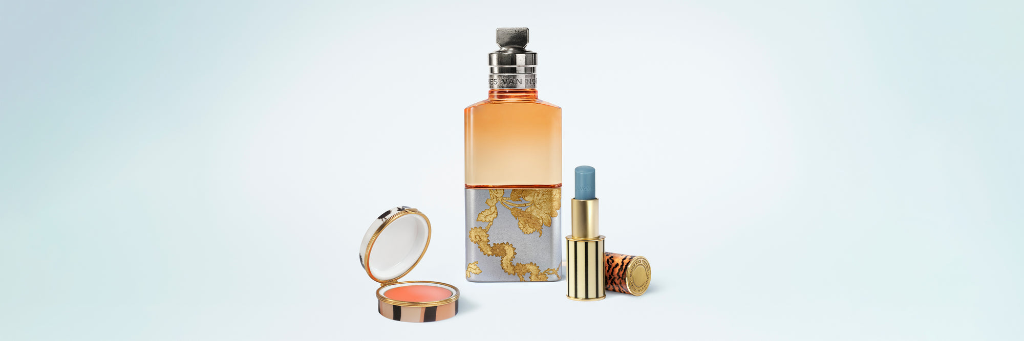 Set of cosmetic products including a perfume bottle, lip box, and lip balm on a light blue background