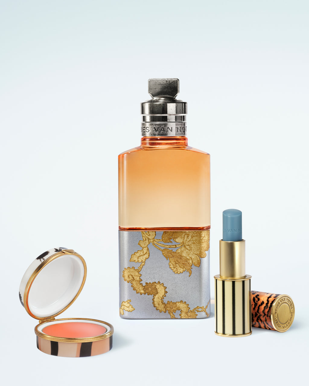 Set of cosmetic products including a perfume bottle, lip box, and lip balm on a light blue background