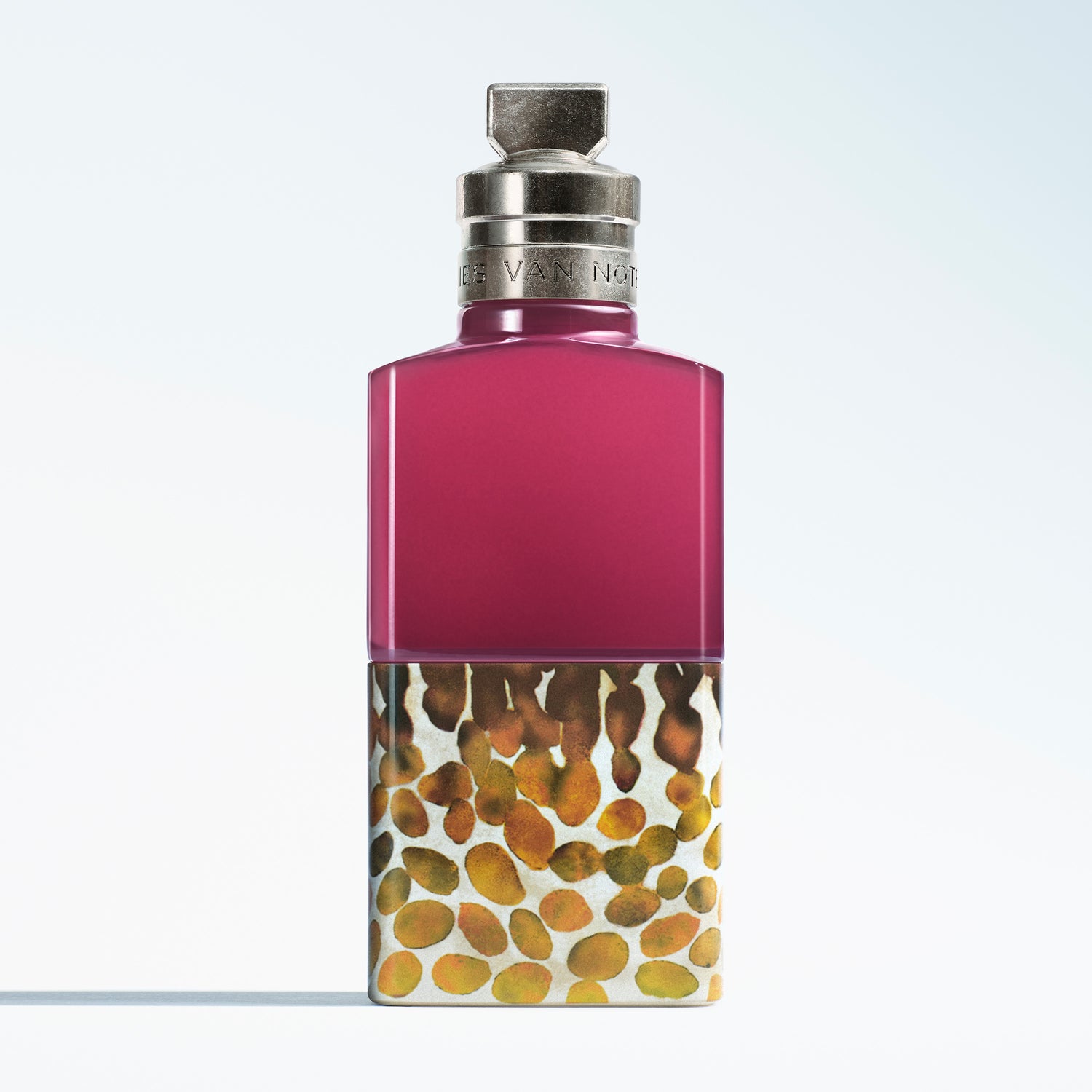 A Dries Van Noten fragrance bottle with a vibrant magenta upper section and a lower section featuring a spotted pattern, topped with a silver cap.