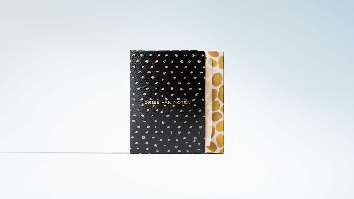 A Dries Van Noten box with a black textured cover patterned with small gold spots and gold lettering on a gradient background.