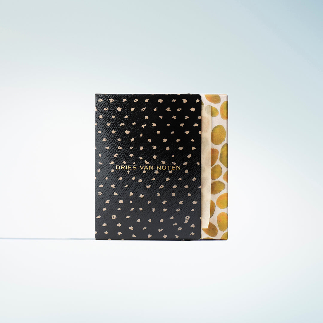 A Dries Van Noten box with a black textured cover patterned with small gold spots and gold lettering on a gradient background.
