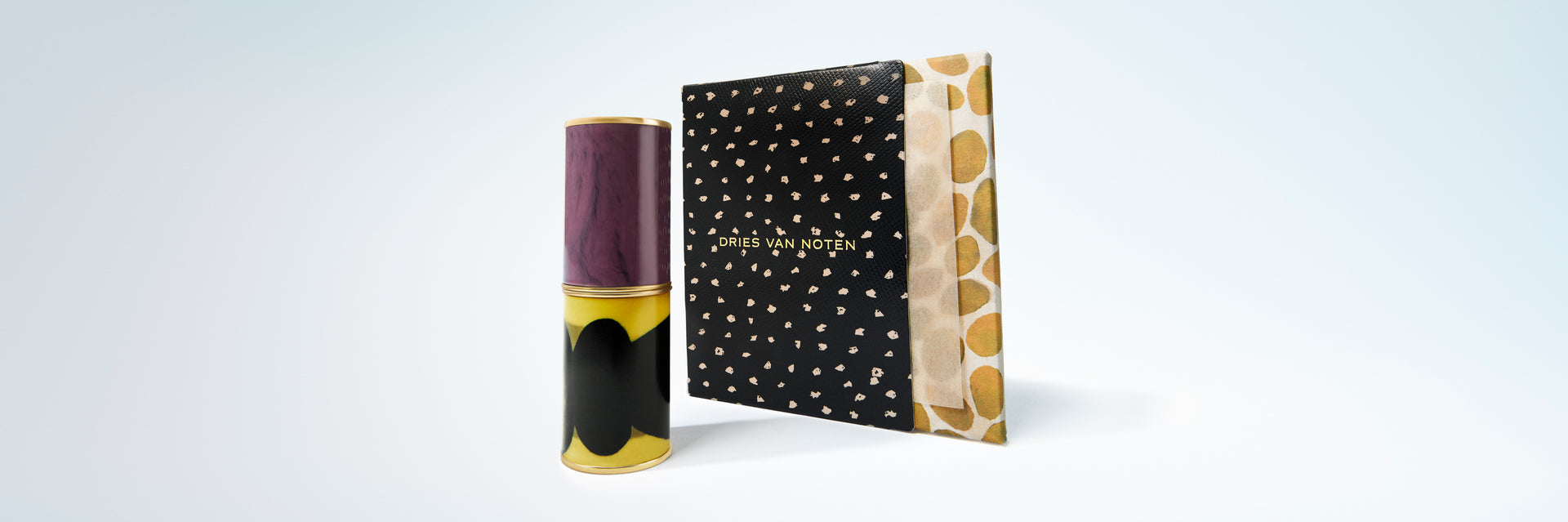 A lipstick case standing next to black and white dotted box with on a gradient background.