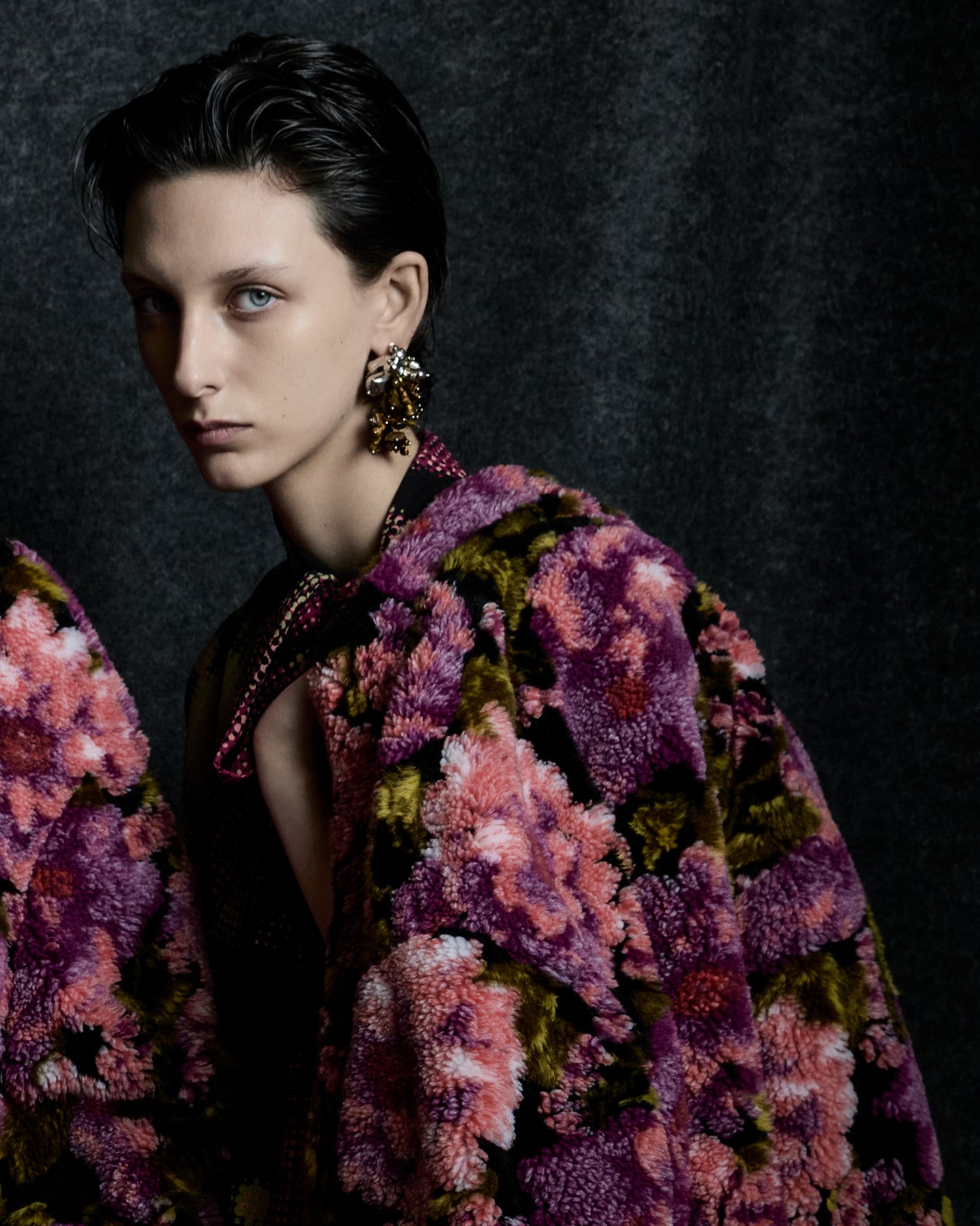Woman wearing a colorful floral-patterned coat against a dark background
