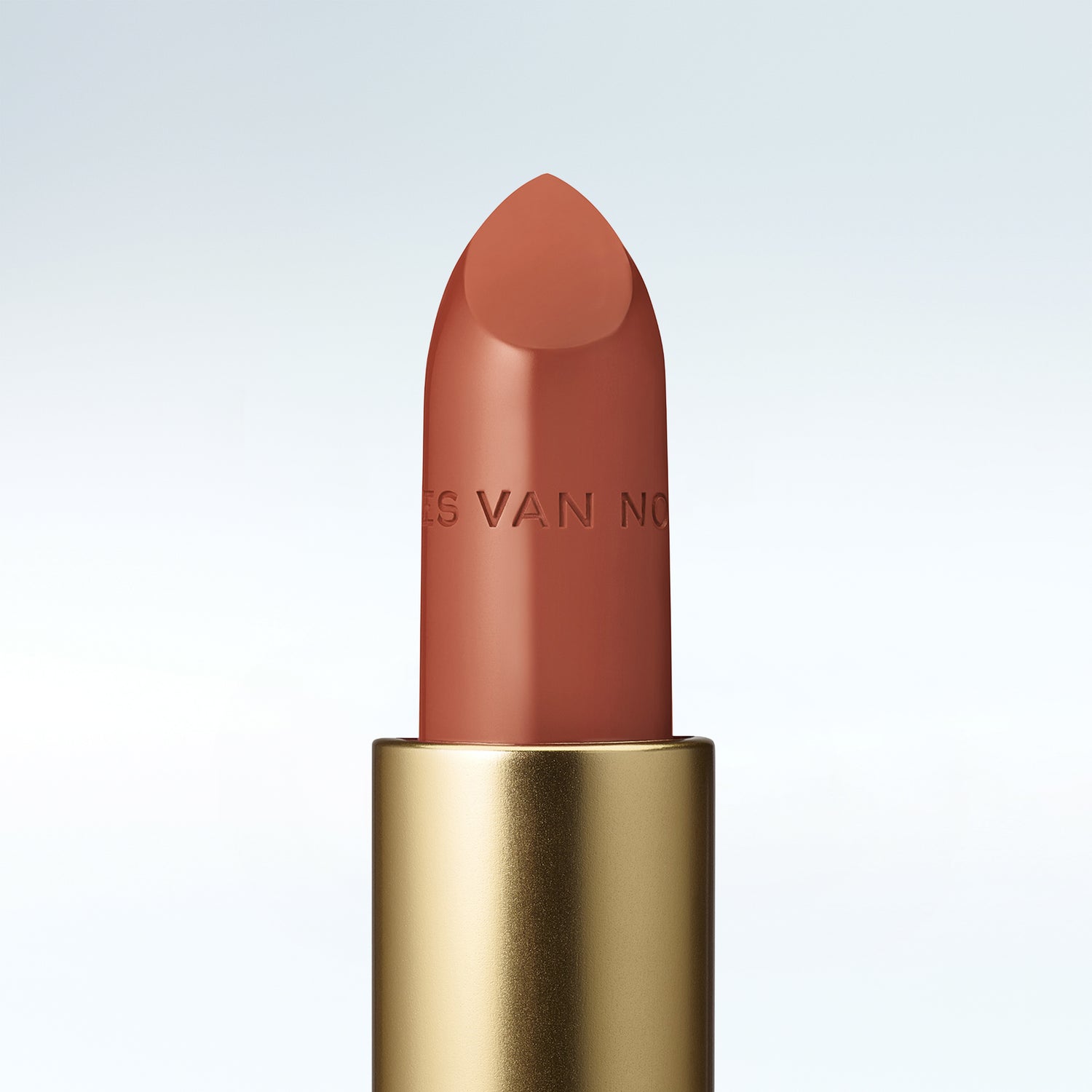 Close-up of a Dries Van Noten lipstick in a gold tube against a cold white background