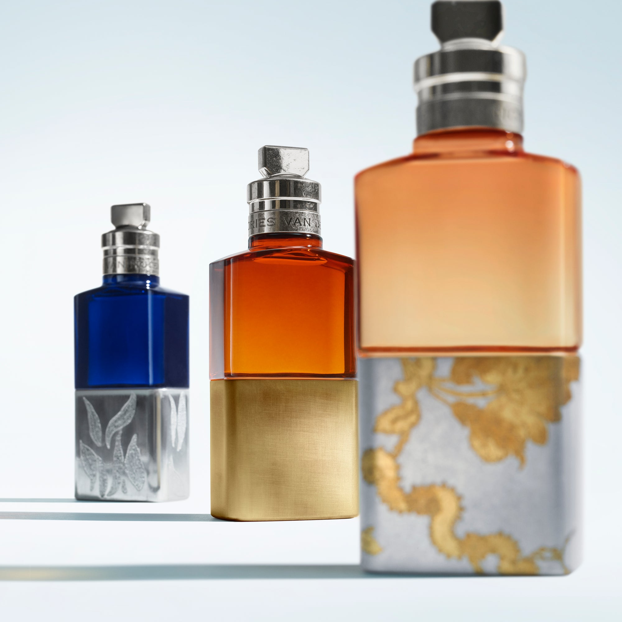 Three perfume bottles with different colored caps on a white background - Dries Van Noten