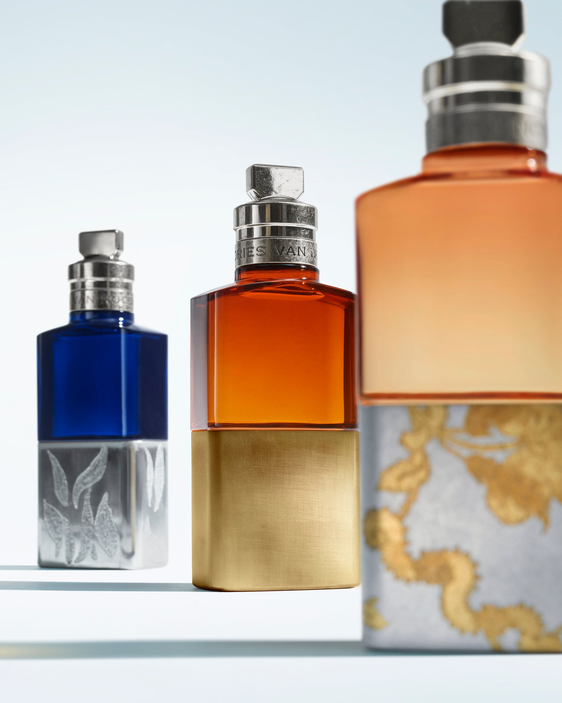 Three perfume bottles of different colors on a light gray background