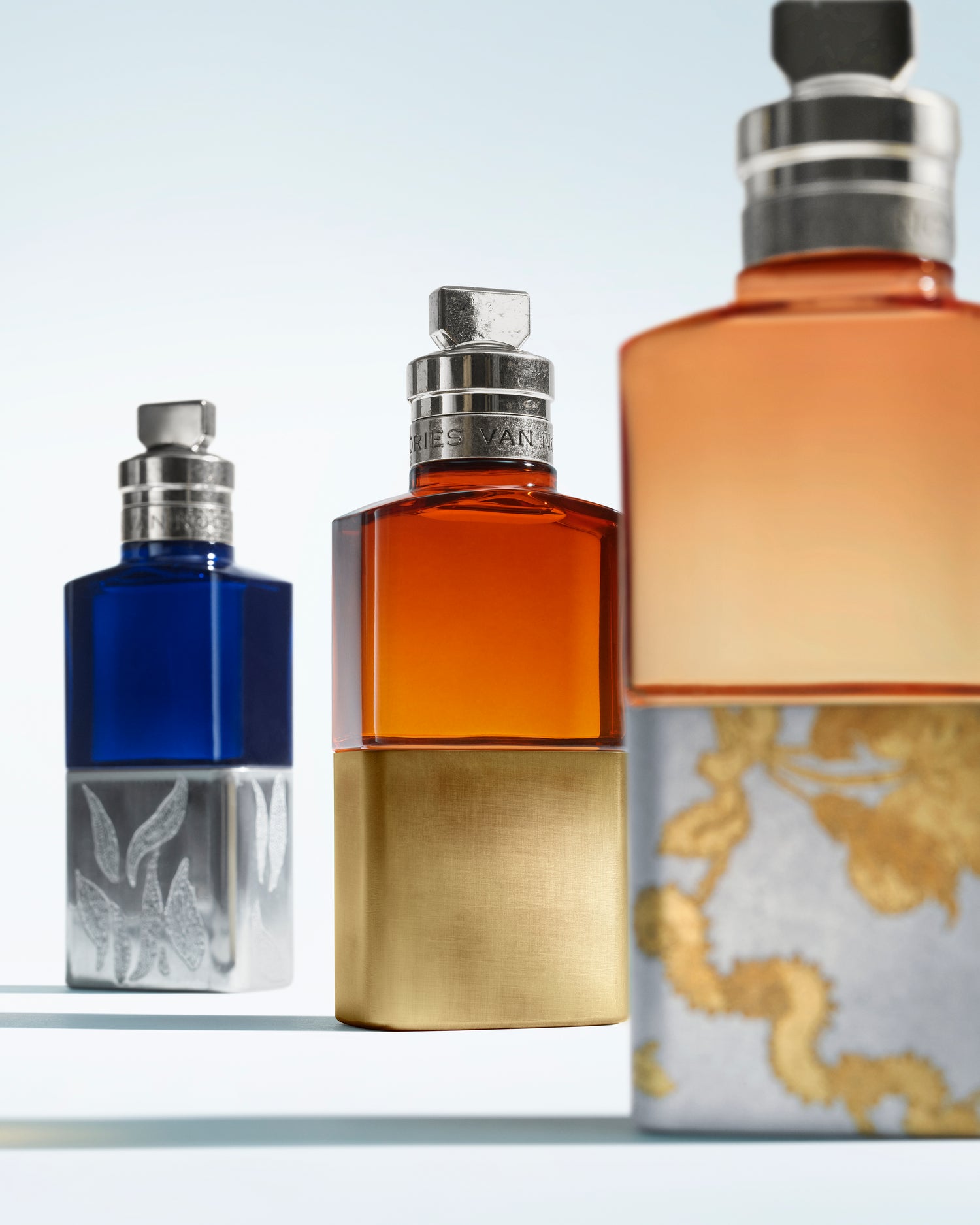 Three perfume bottles of different colors on a light gray background - Dries Van Noten
