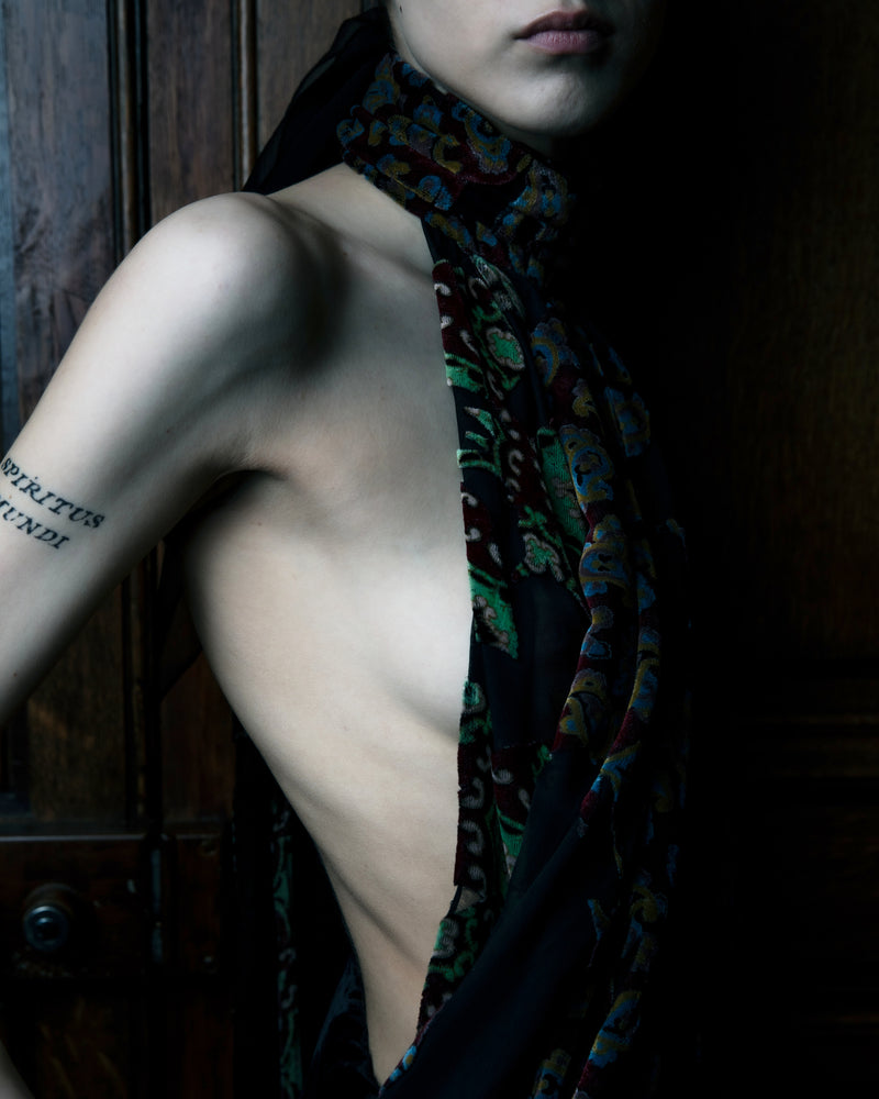 Partial nude body with a patterned scarf draped over shoulders against a dark background