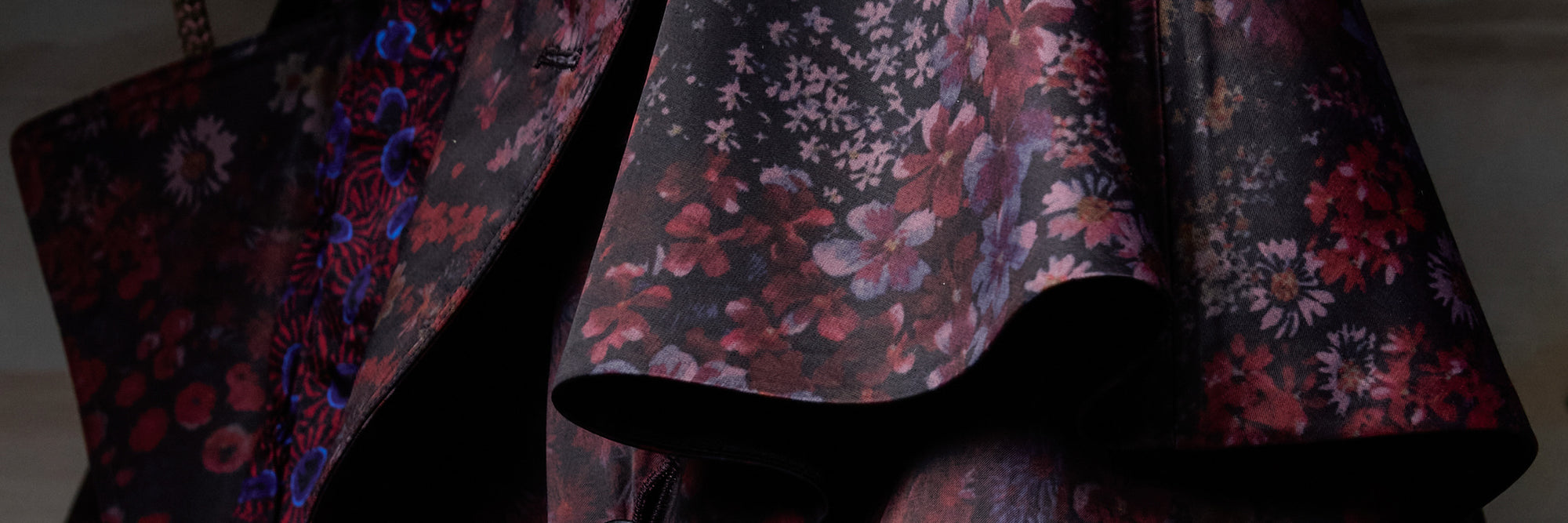 A close-up of a dark floral coat  featuring a black base with red, pink and purple flowers.