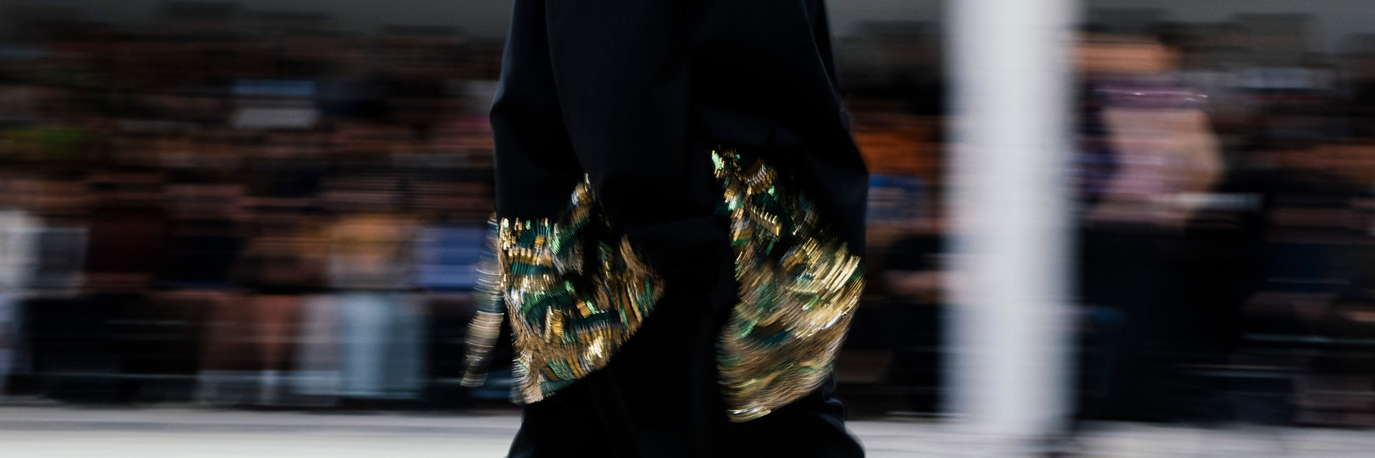 Close-up of a person wearing a black outfit with gold and green embroidery accents on a blurred background