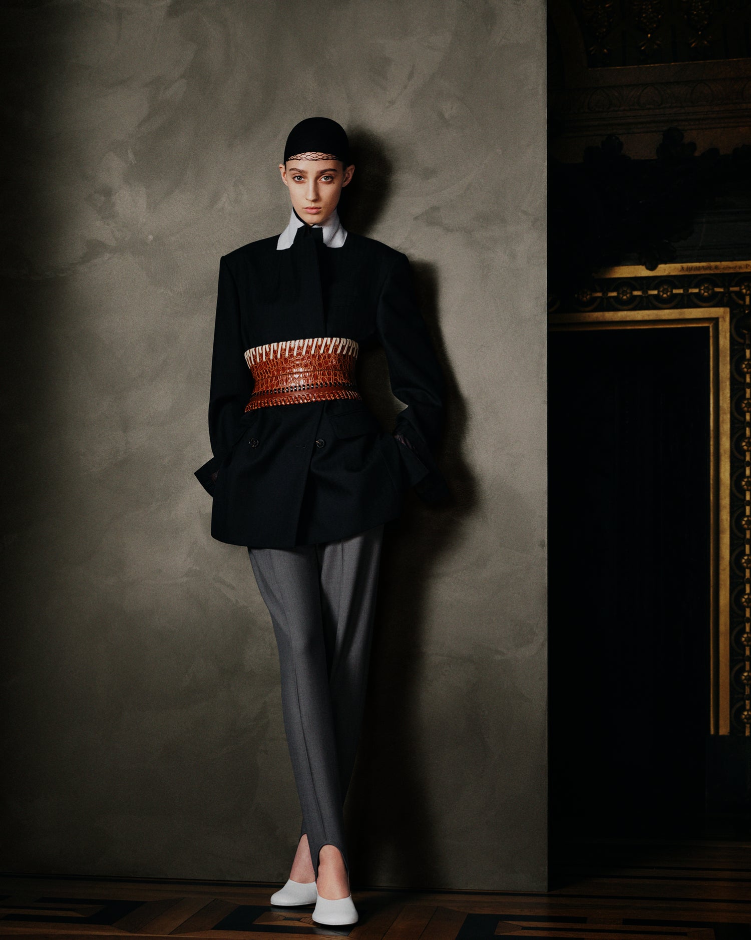 Person wearing a black outfit with a textured wall and decorative elements in the background