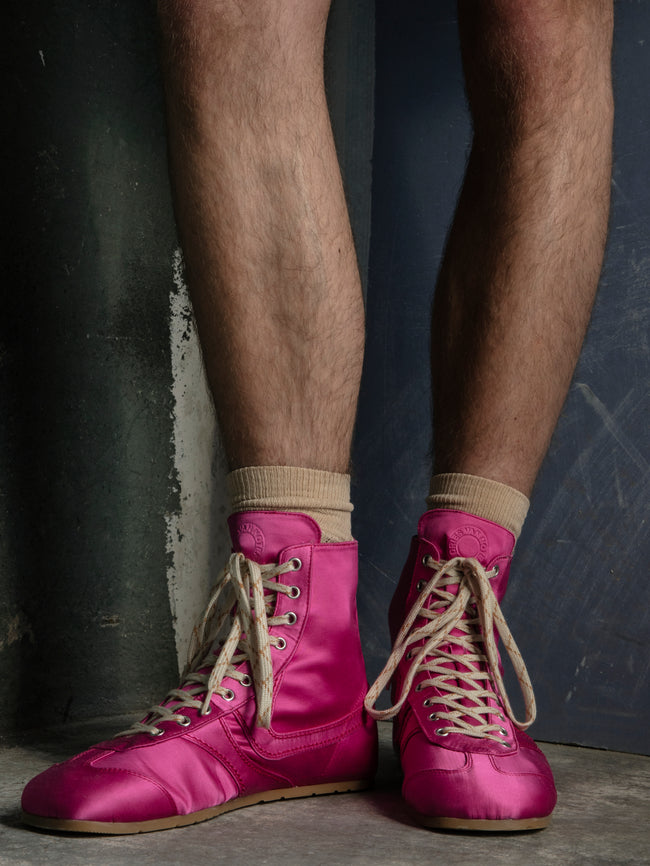 Person wearing bright pink high-top sneakers with beige laces against a dark wall.