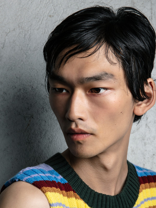 Man wearing a colorful striped sweater against a gray concrete wall