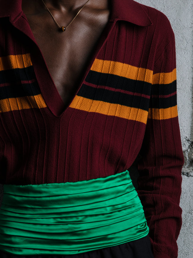 Person wearing a maroon sweater with yellow and black stripes and a green top against a concrete wall.