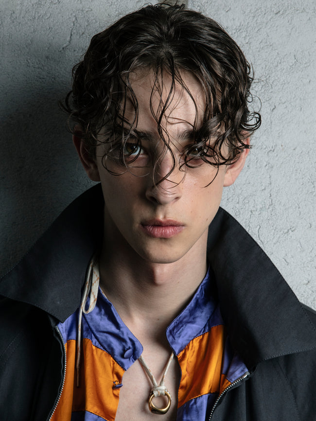 Person wearing a black jacket with orange and blue interior, against a gray textured wall.