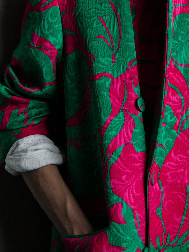 Close-up of a person wearing a vibrant pink and green patterned coat against a gray background