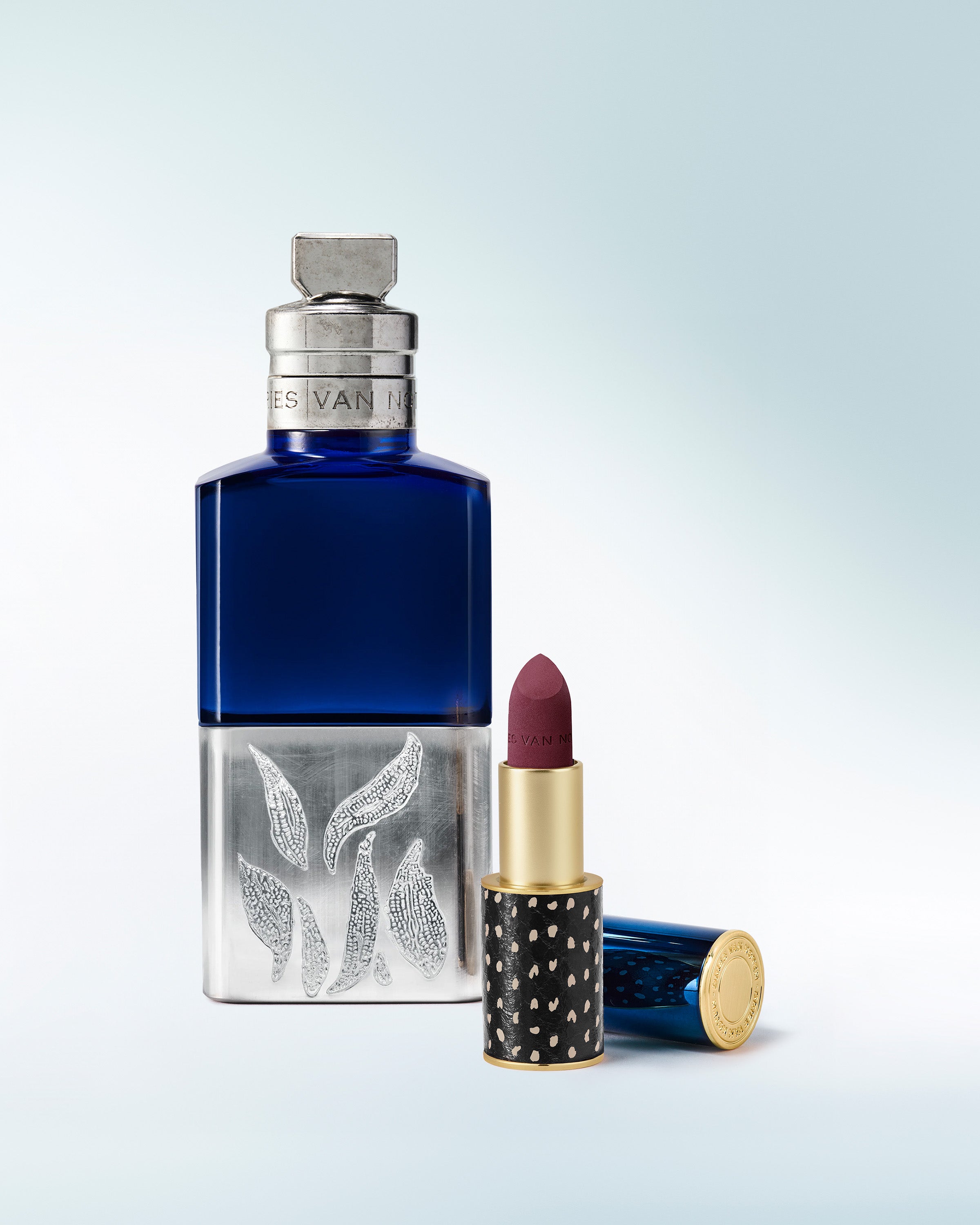 Blue perfume bottle and red lipstick with decorative packaging on a light gray background - Dries Van Noten
