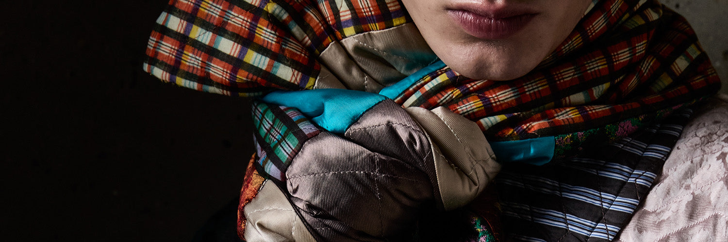 A close-up of a person wearing a multicolor plaid scarf  with a bright turquoise lining, set against a dark background.