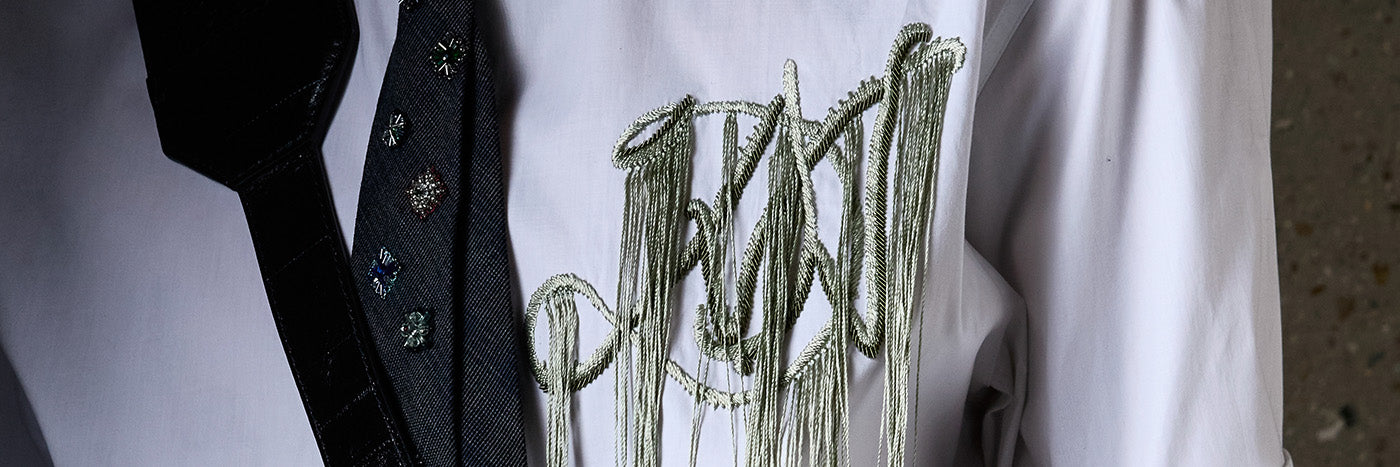 Close-up of a white shirt with green embroidery and a dark patterned tie.