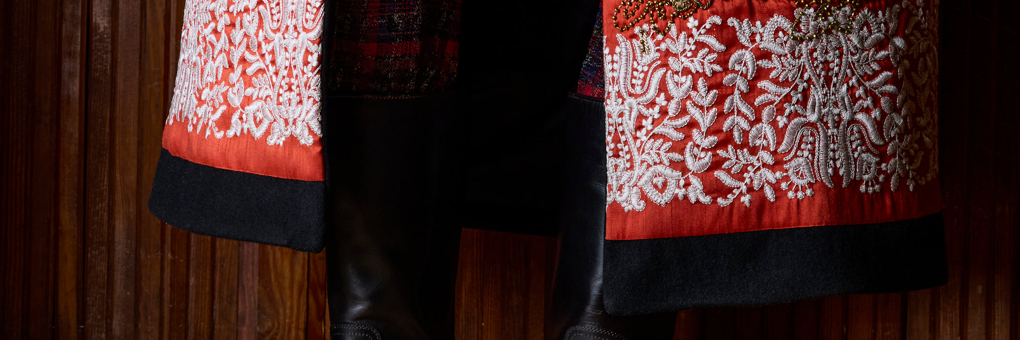 Close-up of a black garment with wide red and white embroidered borders, shown against a dark wood background.