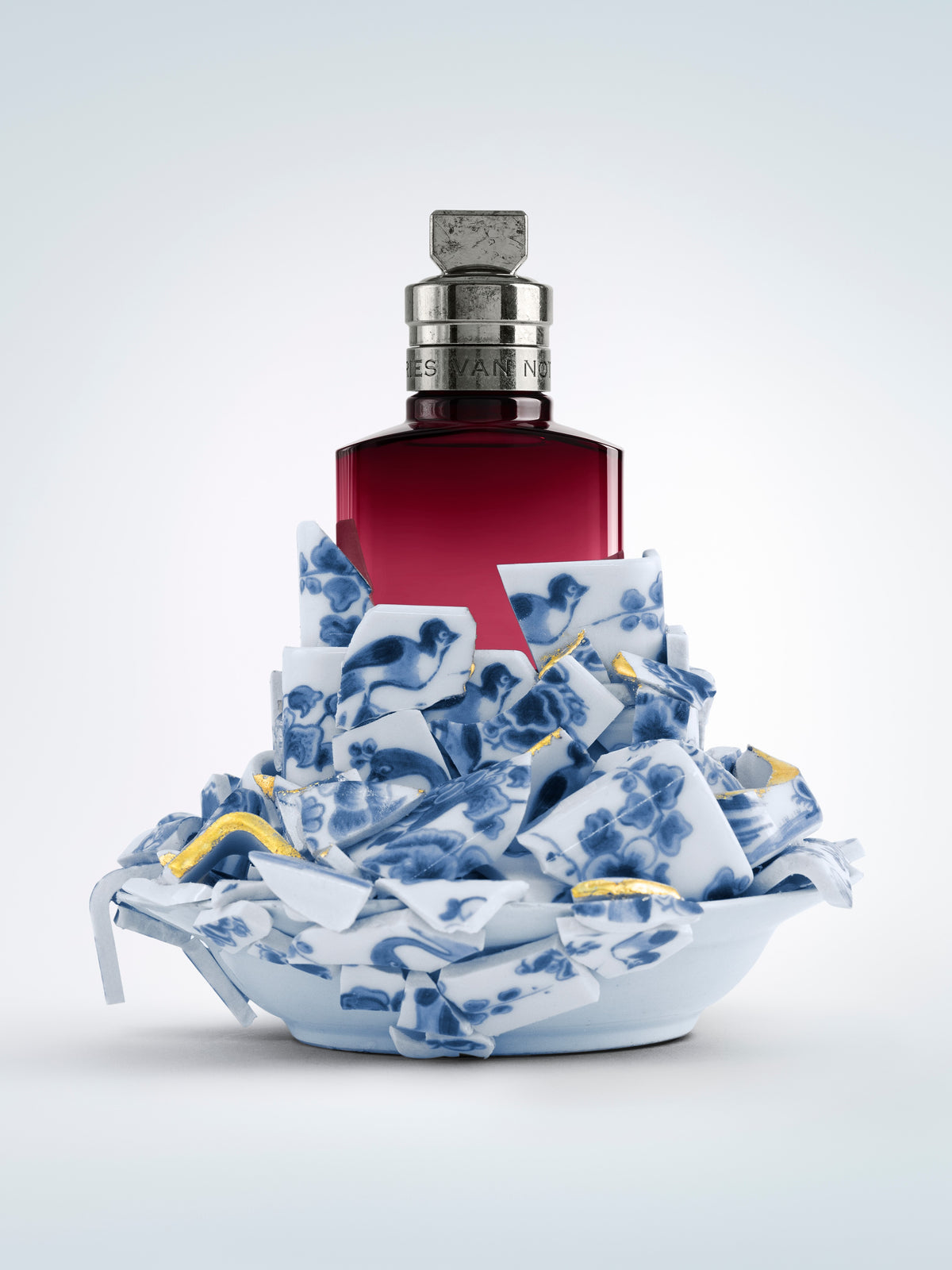 Bottle with a red label on a decorative blue and white ceramic base against a light gray background - Dries Van Noten