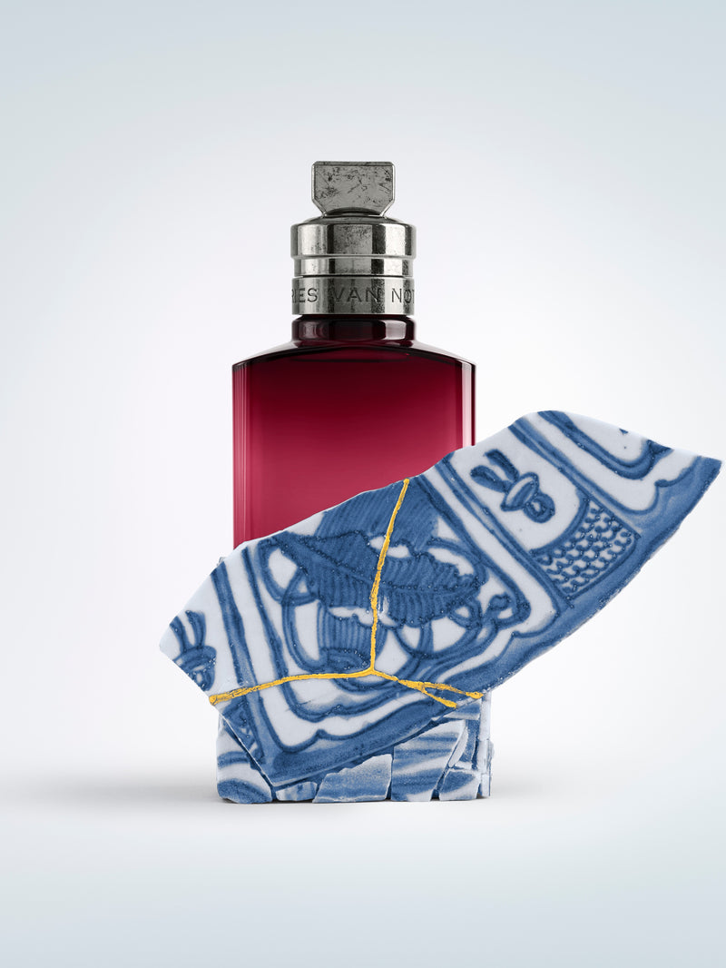 Red perfume bottle with a blue and white patterned cloth on a light gray background - Dries Van Noten