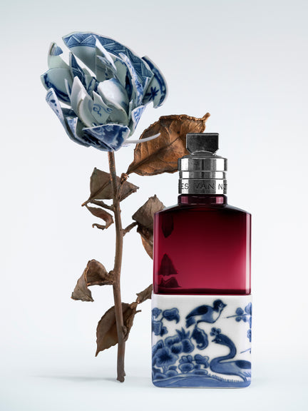 Perfume bottle with blue floral design next to a dried flower on a white background - Dries Van Noten