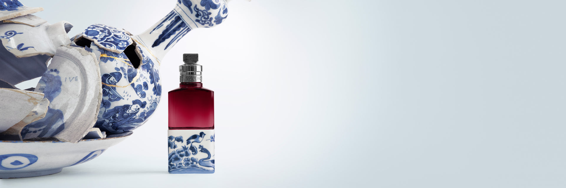 Perfume bottle with blue and white design next to a ceramic vase on a light gray background - Dries Van Noten