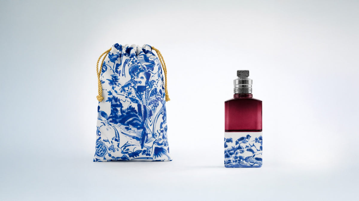 Perfume bottle with blue floral design next to a dried flower on a white background - Dries Van Noten