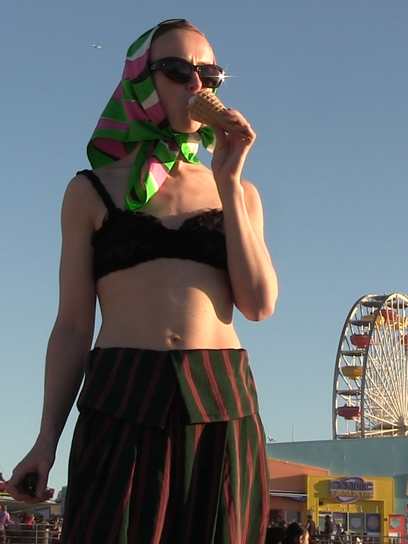 Woman eating an ice cream cone with a colorful headscarf and black sungalsses, Ferris wheel in the background