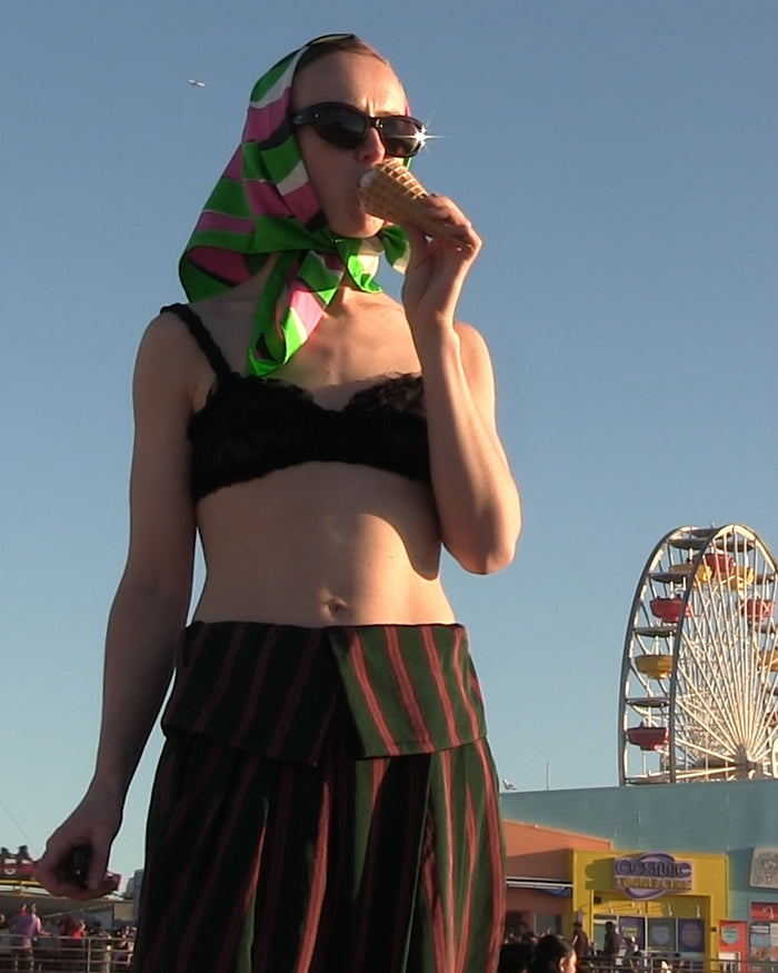 Woman eating an ice cream cone with a colorful headscarf and black sungalsses, Ferris wheel in the background