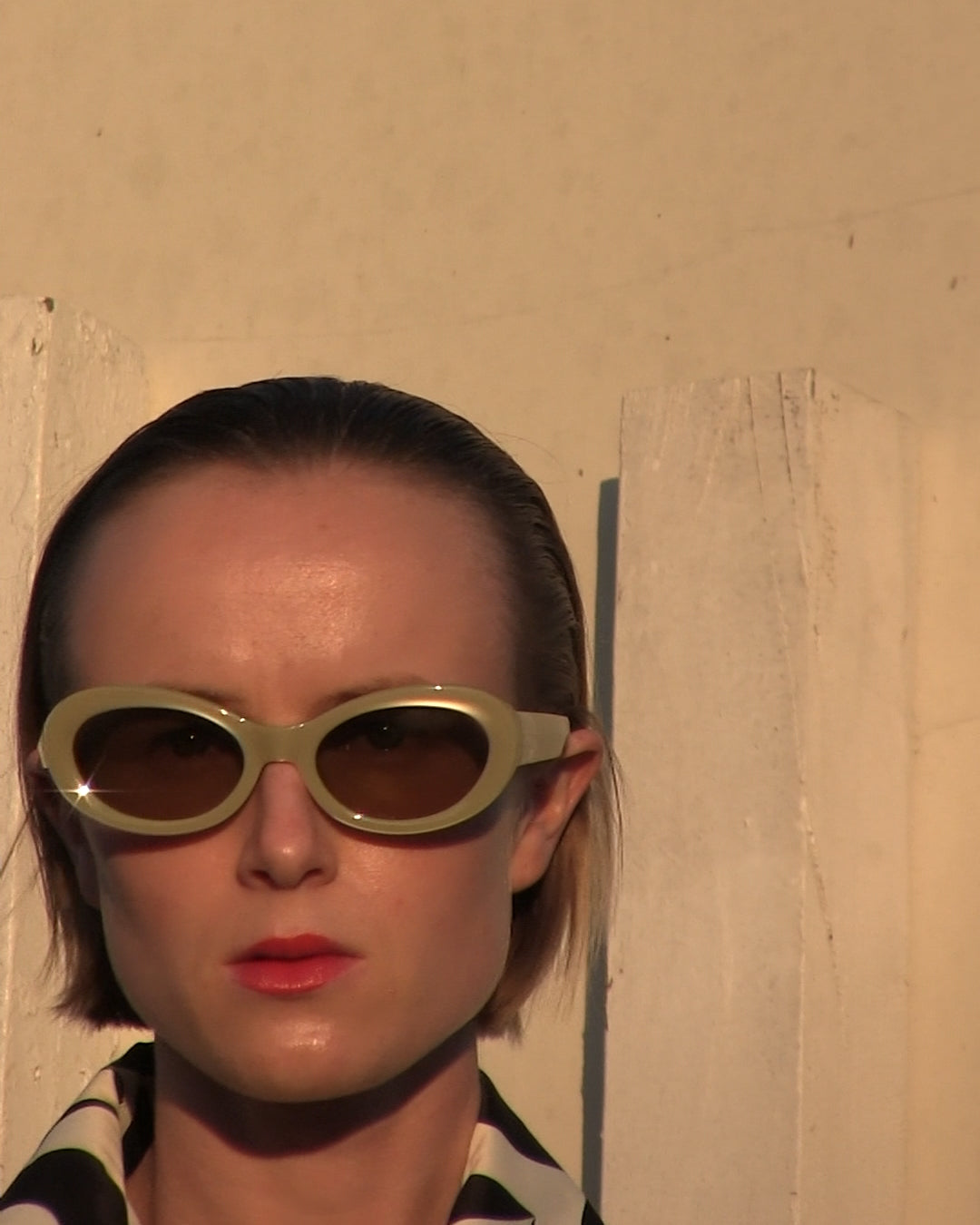 Person wearing oval sunglasses with a neutral background