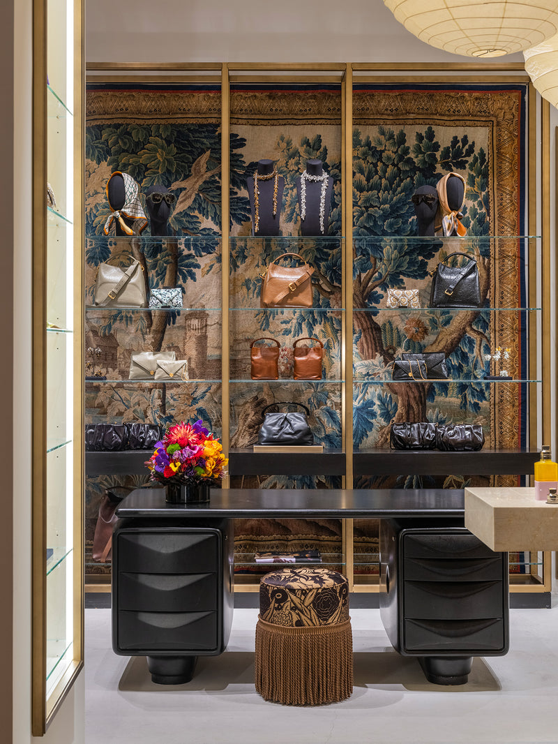 A luxury interior scene featuring a large wall-mounted glass display cabinet with gold framing, filled with handbags and accessories. 
