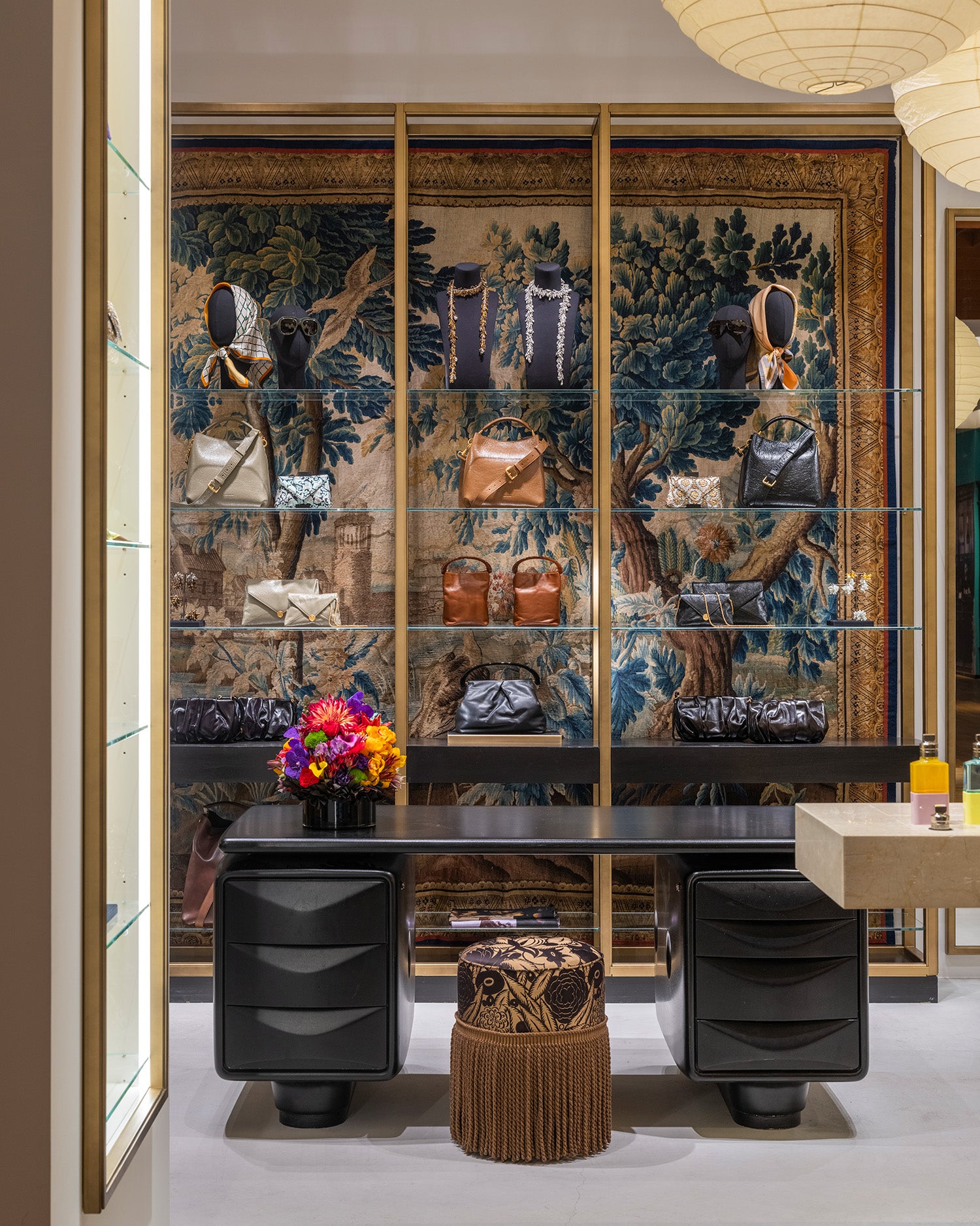 A luxury interior scene featuring a large wall-mounted glass display cabinet with gold framing, filled with handbags and accessories. 