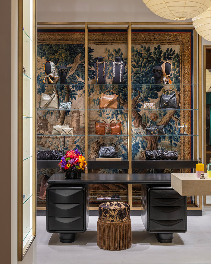 A luxury interior scene featuring a large wall-mounted glass display cabinet with gold framing, filled with handbags and accessories. 