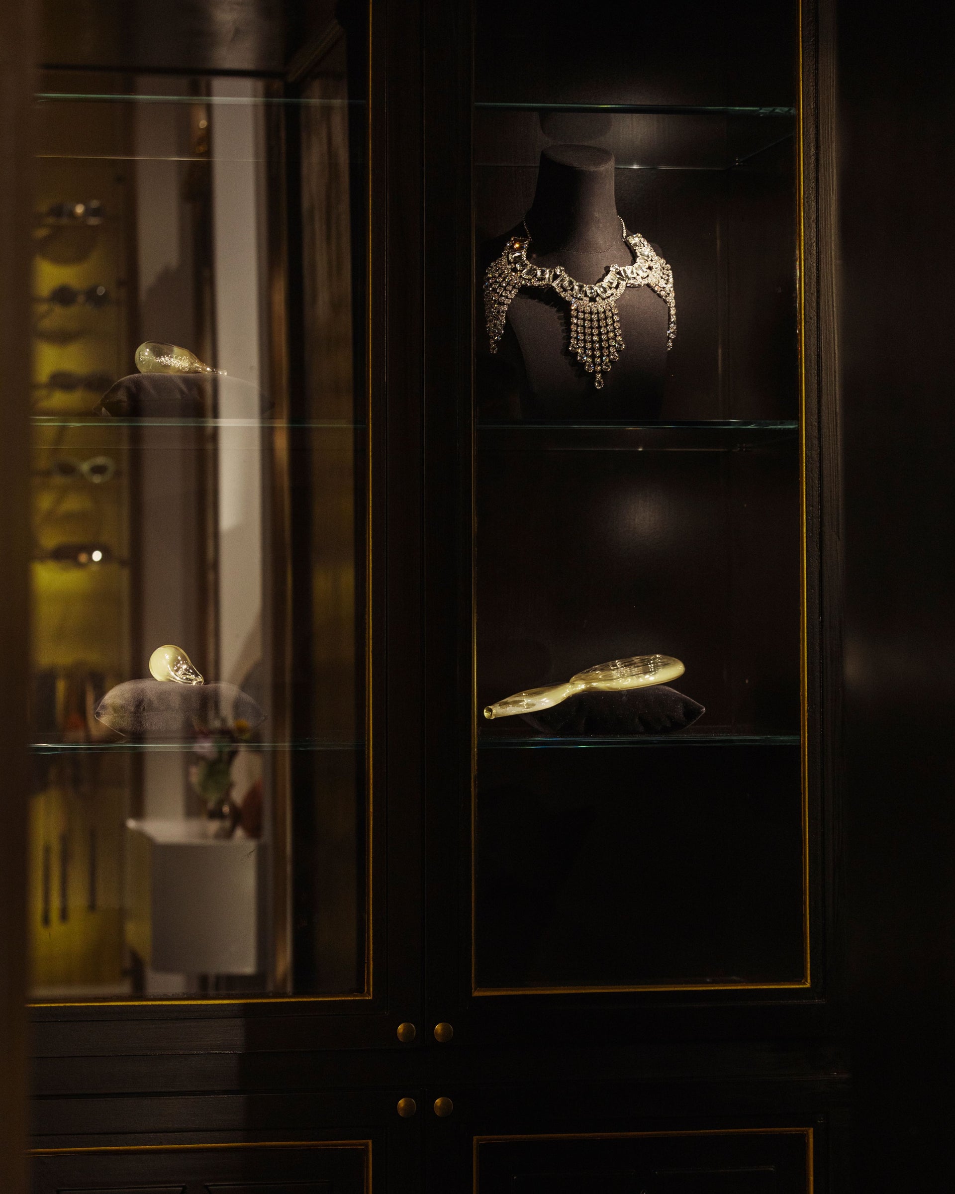 Glass display cabinet with jewelry pieces, including a necklace and small objects, lit against a dark background 