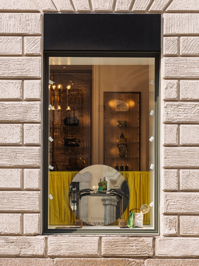 Store window display with a mirror reflecting interior decor, framed by a stone wall.