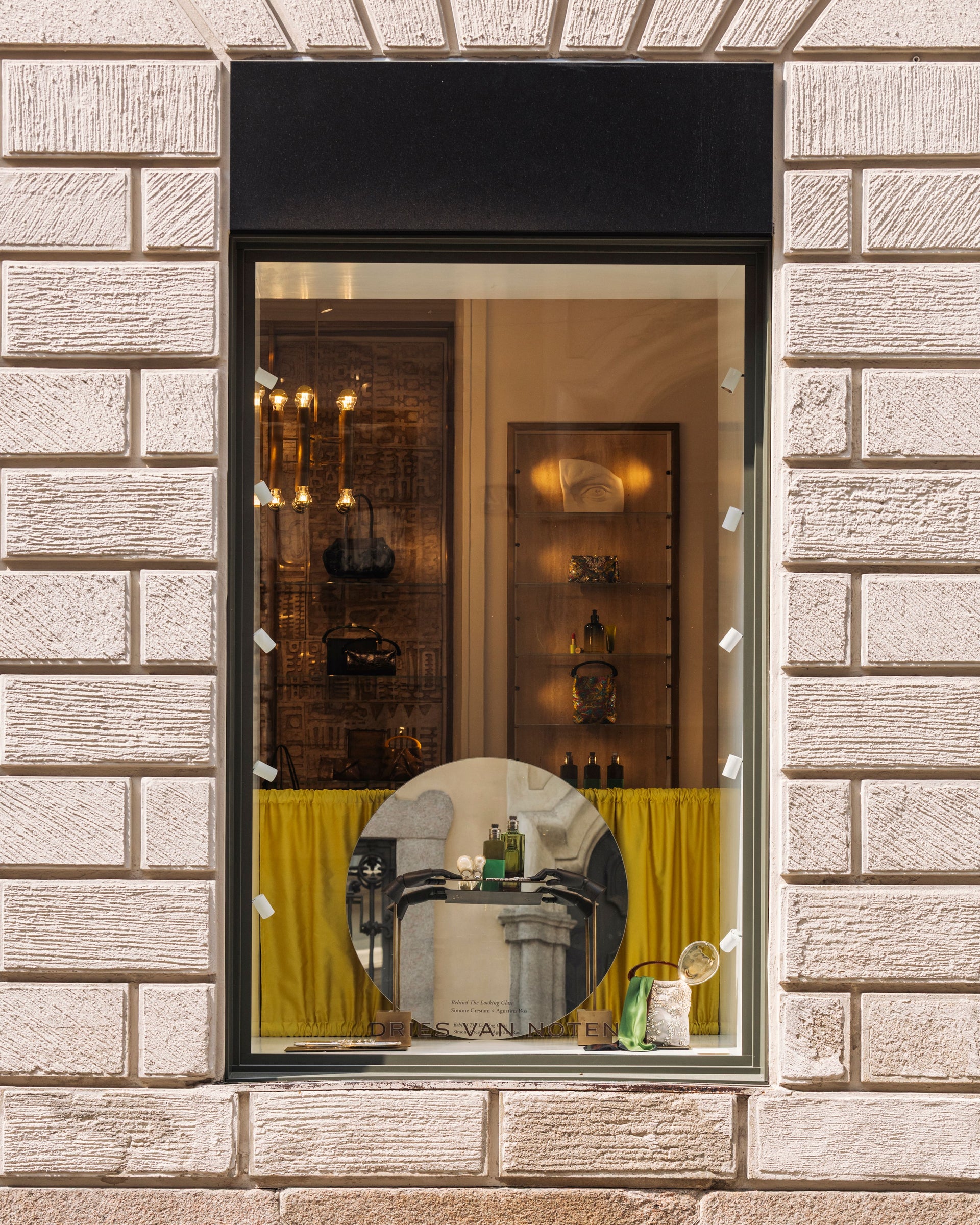 Store window display with a mirror reflecting interior decor, framed by a stone wall.
