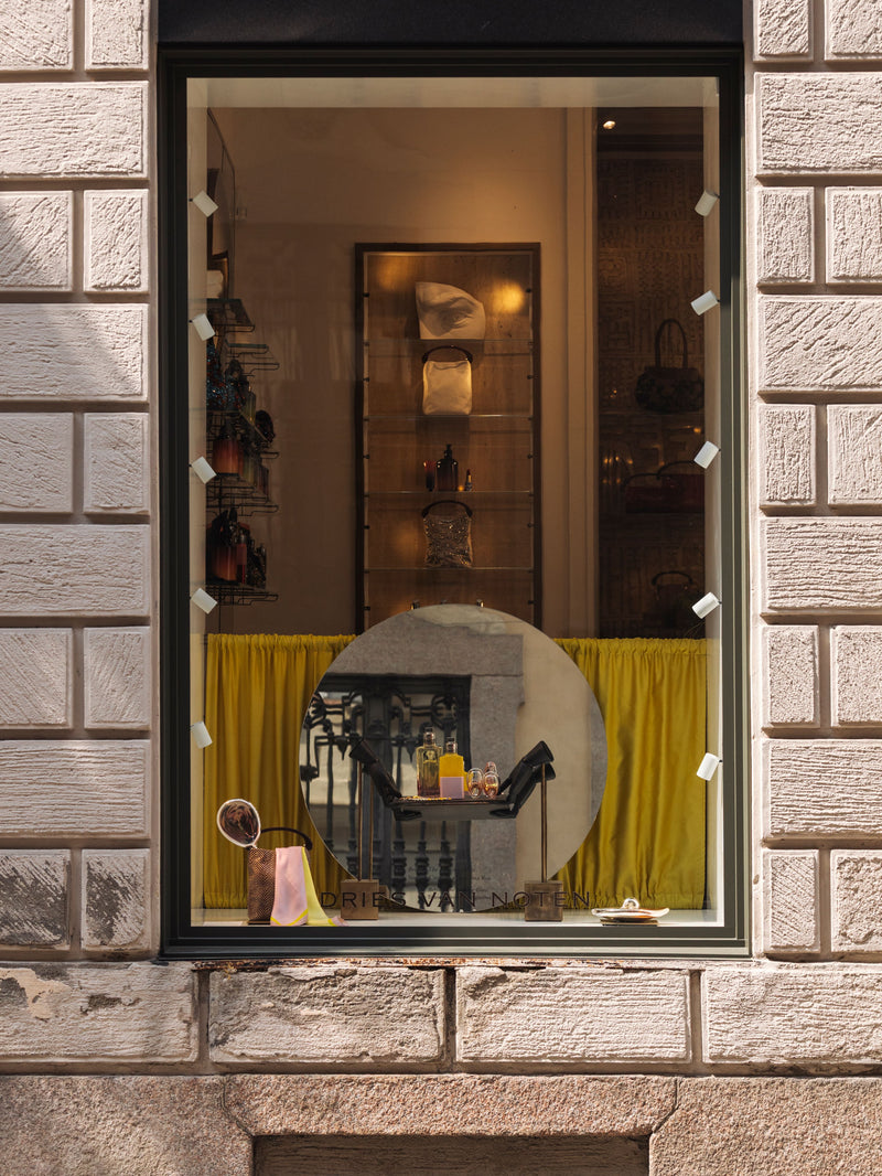 Store window display with a yellow curtain and various items on a stone building facade.