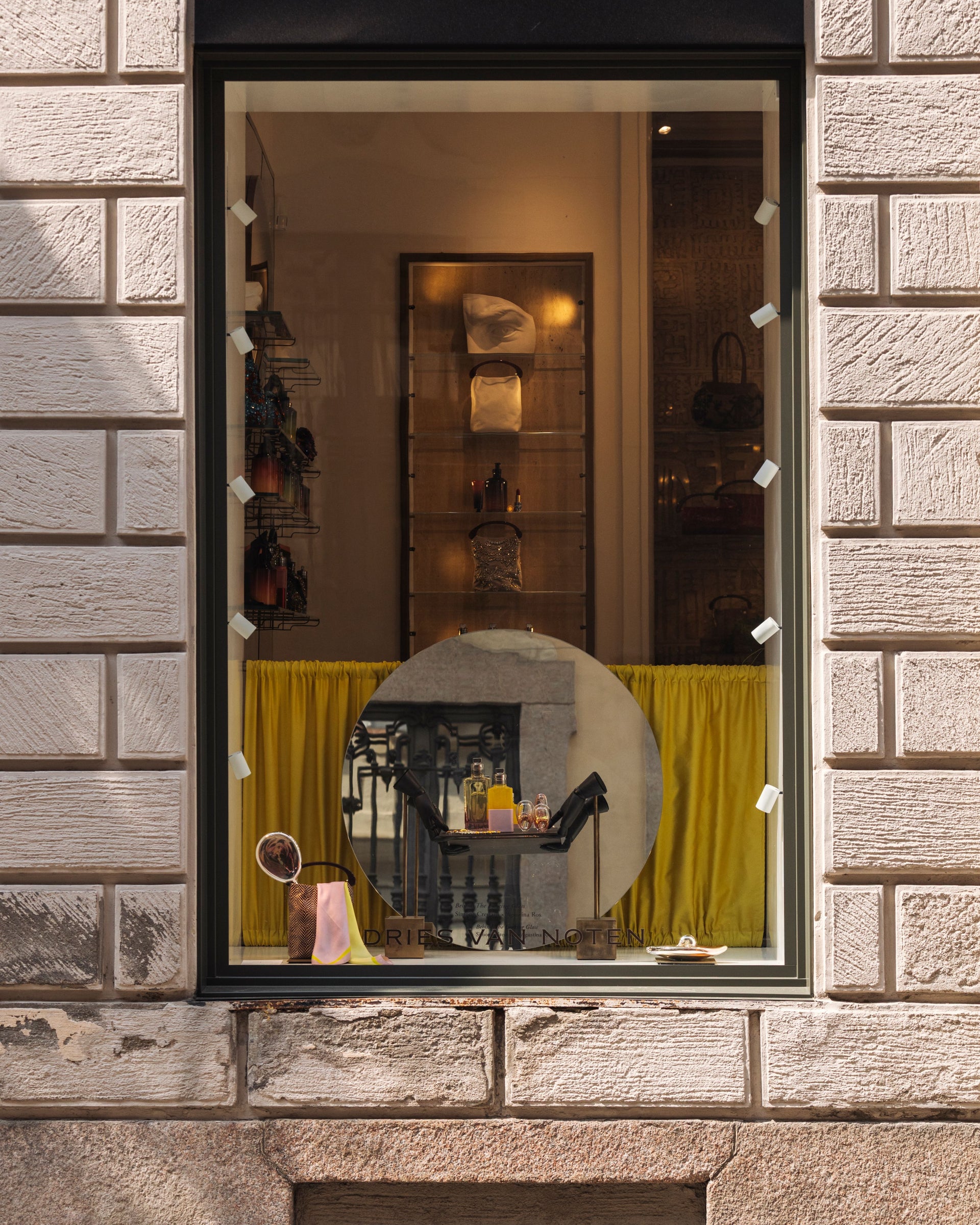 Store window display with a yellow curtain and various items on a stone building facade.