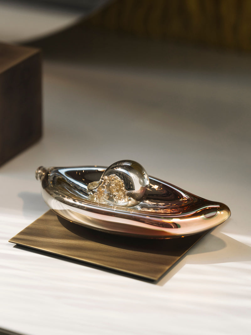 Abstract metallic decorative object with a rounded form and gold detail, displayed on a small platform 