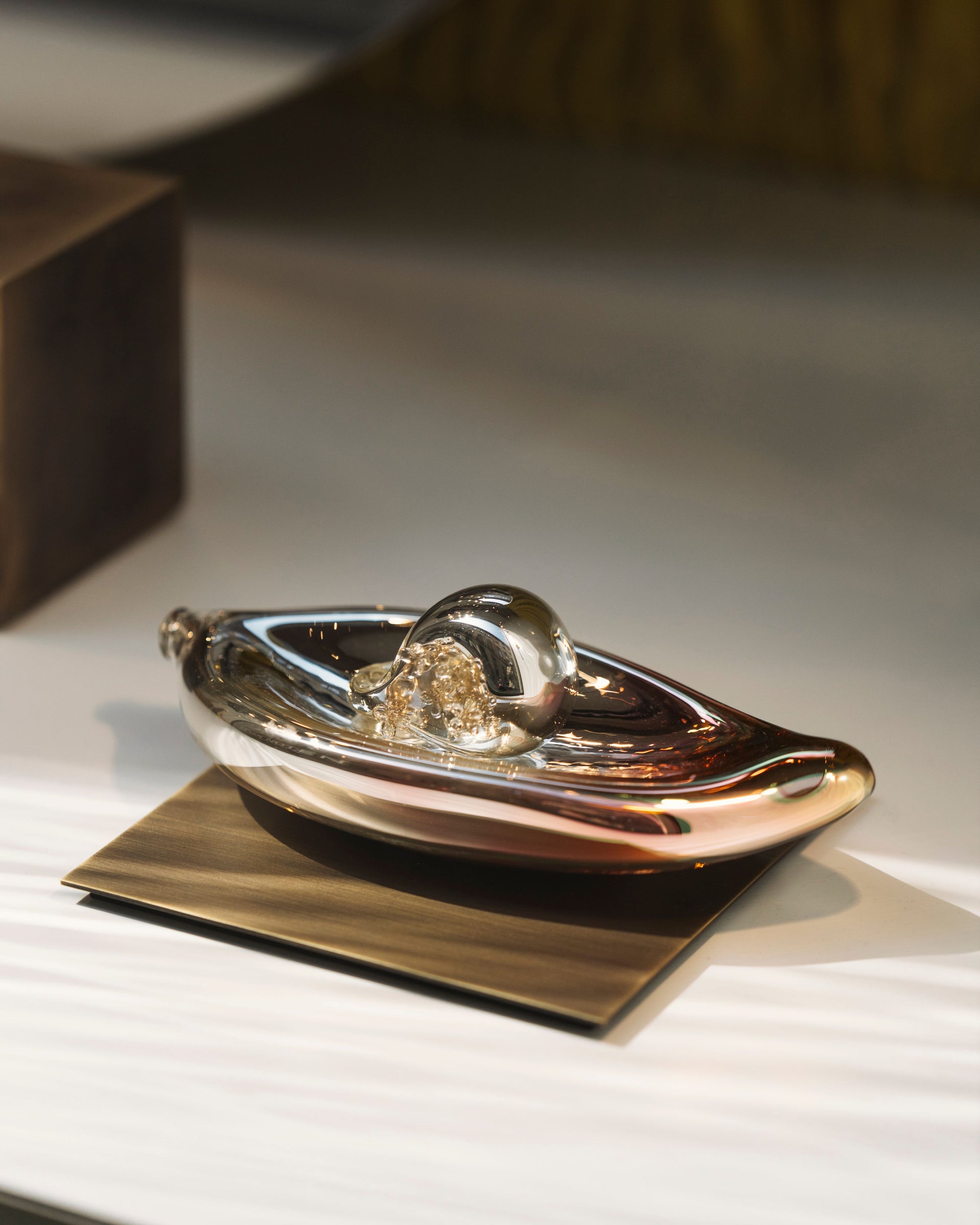 Abstract metallic decorative object with a rounded form and gold detail, displayed on a small platform 