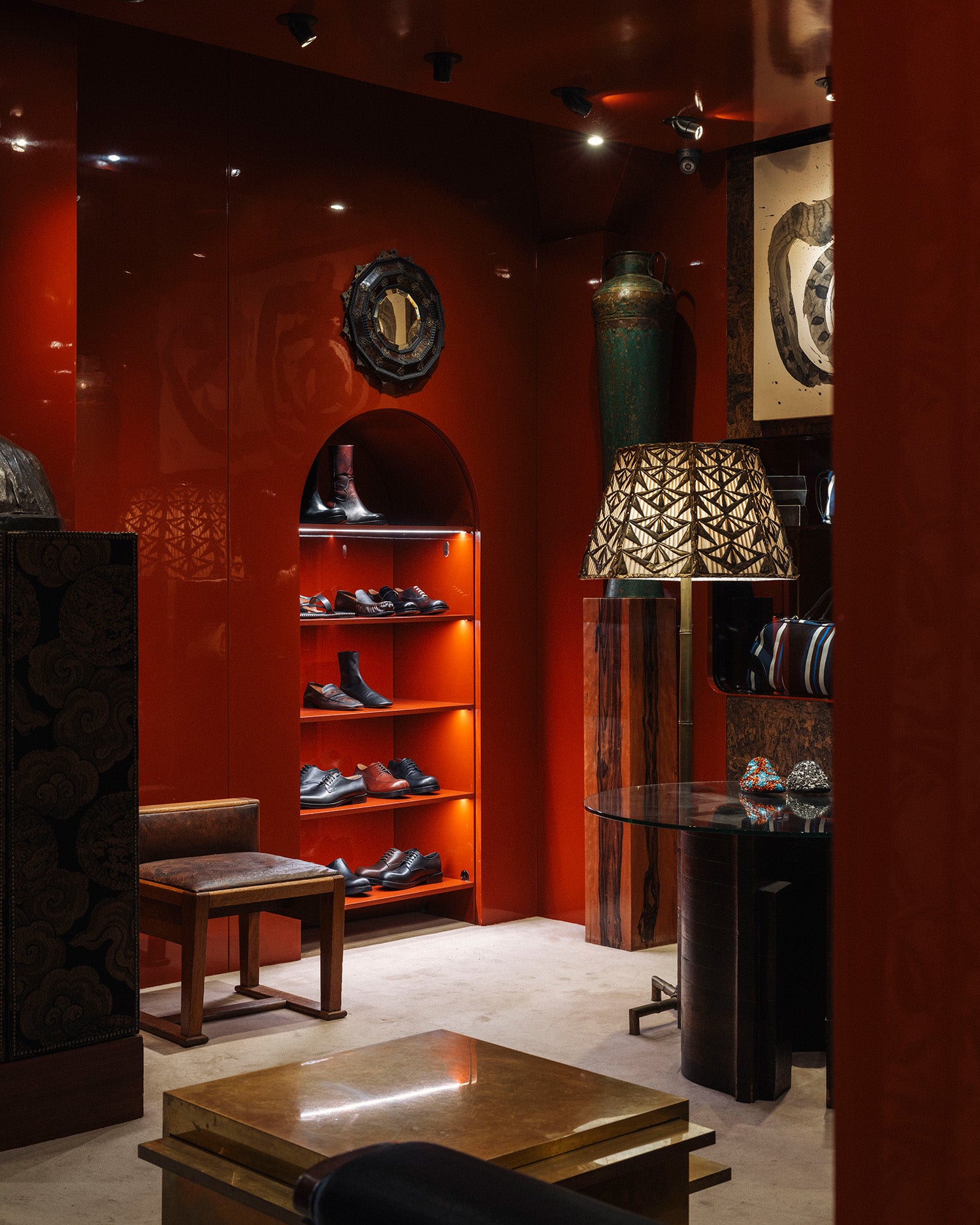 A luxury interior display featuring a red leather booth with a brown leather seat, a patterned gold and brown floor lamp, and a glass-topped table in a richly decorated red boutique.