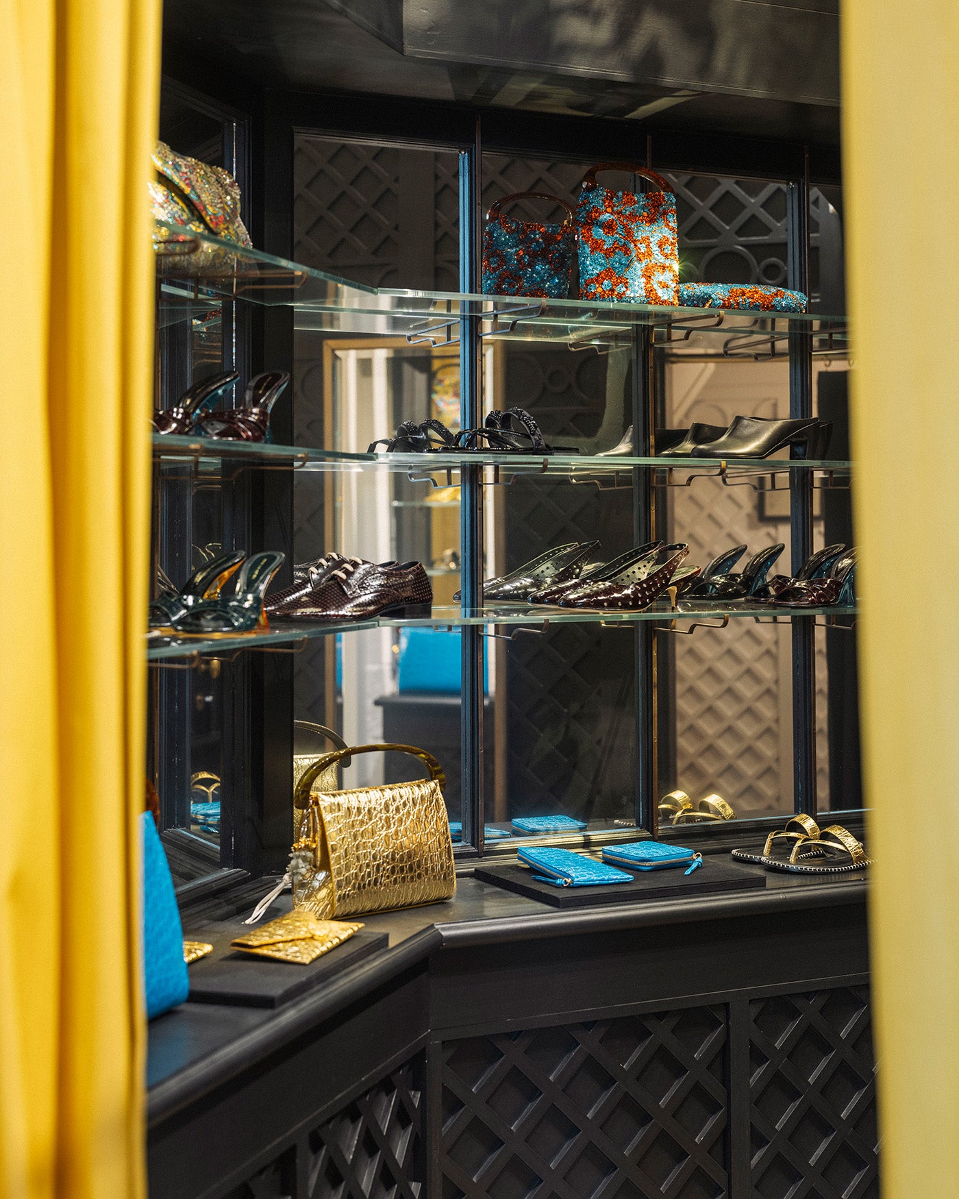 A luxury display shelf in a black room showcasing designer handbags and shoes, framed by a bright yellow curtain on the left and right. 