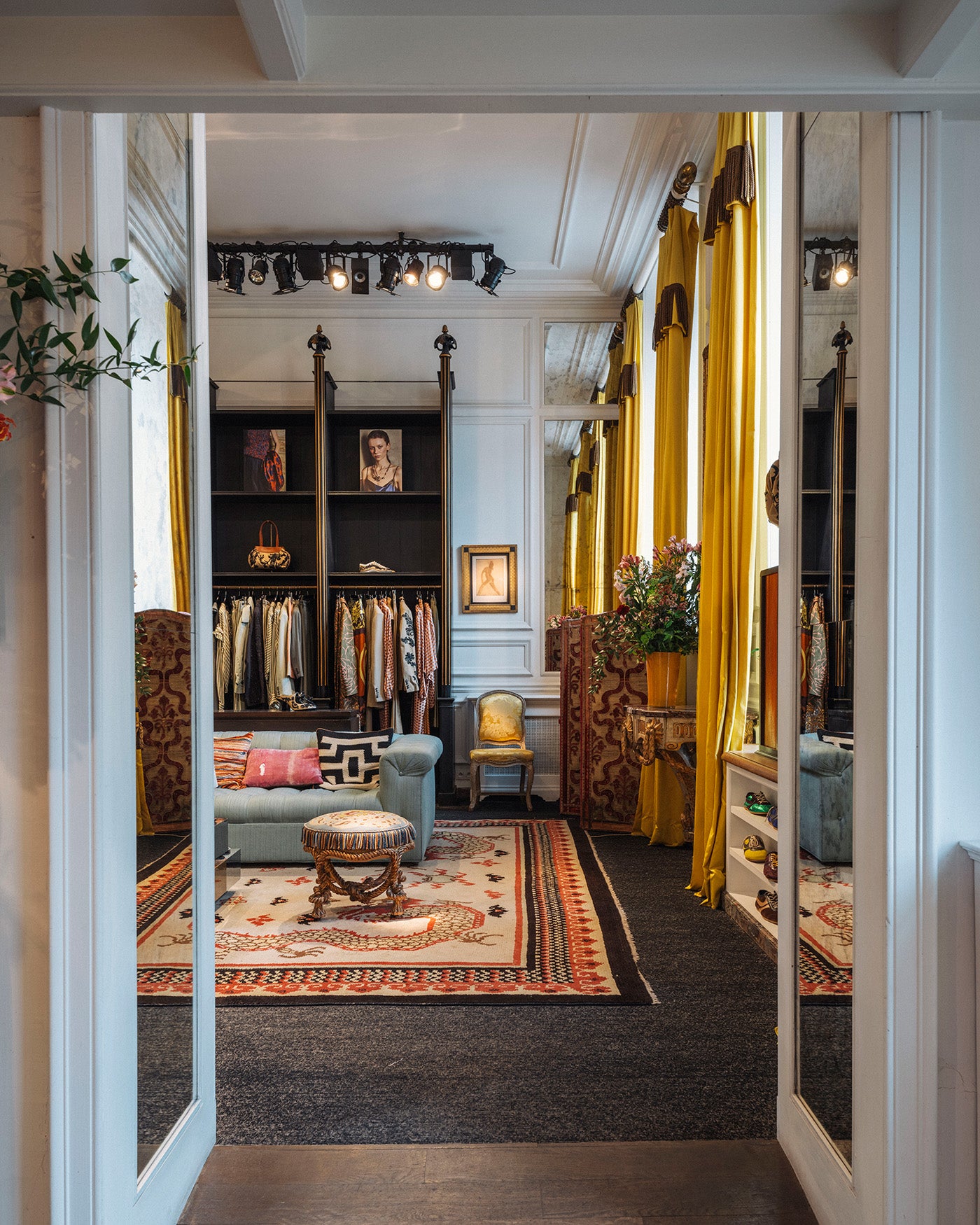 A luxurious walk-in interior with bright yellow drapes, dark wood shelving, a light blue sofa with patterned pillows, a patterned area rug, and warm ambient lighting.
