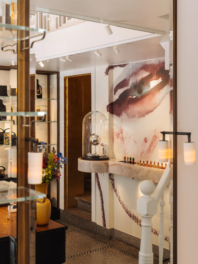 Store interior, featuring a lipstick display, decorative elements, a wall painting and a shelve with handbags and jewellery in the background.