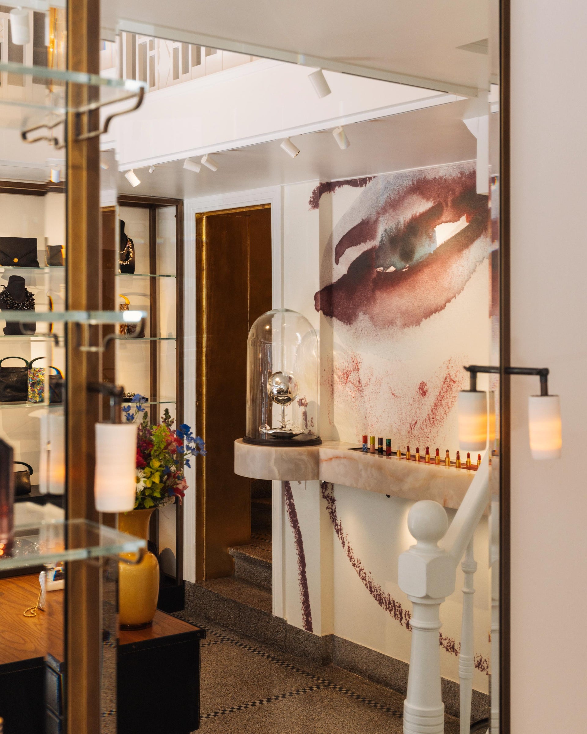 Store interior, featuring a lipstick display, decorative elements, a wall painting and a shelve with handbags and jewellery in the background.