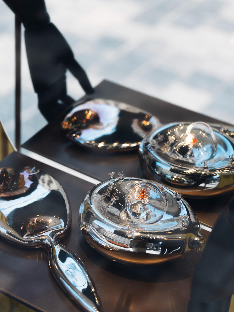 Artistic renditions of a mirror and dish made of glass placed on a black surface, in front of a mirror. 