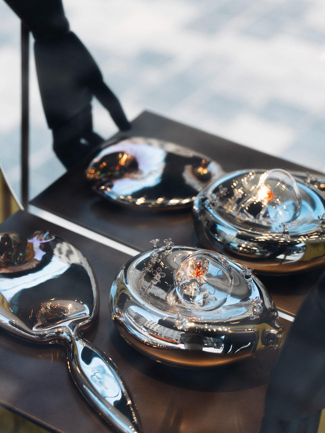 Artistic renditions of a mirror and dish made of glass placed on a black surface, in front of a mirror. 